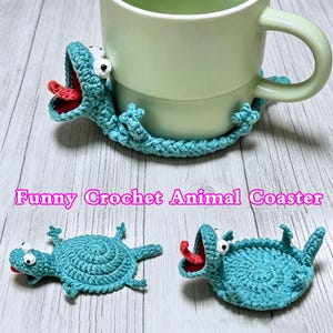May include: A light blue crochet animal coaster shaped like a lizard with a wide-open mouth, a red tongue, and white eyes. The coaster is shown wrapped around a light green mug and also displayed flat. The text Funny Crochet Animal Coaster is visible.