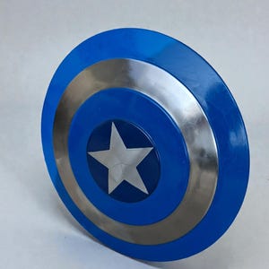 May include: A blue and silver shield with a white star in the center. The shield has a circular design with a blue outer ring, a silver middle ring, and a blue center with a white star.