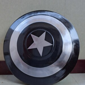 May include: A circular shield in black and silver, featuring a central silver star. The shield has a glossy finish and a design of concentric rings. The central star is a five-pointed design.