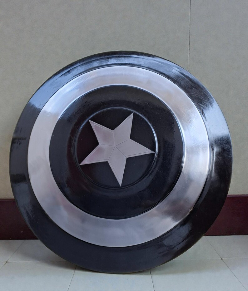 May include: A circular shield in black and silver, featuring a central silver star. The shield has a glossy finish and a design of concentric rings. The central star is a five-pointed design.