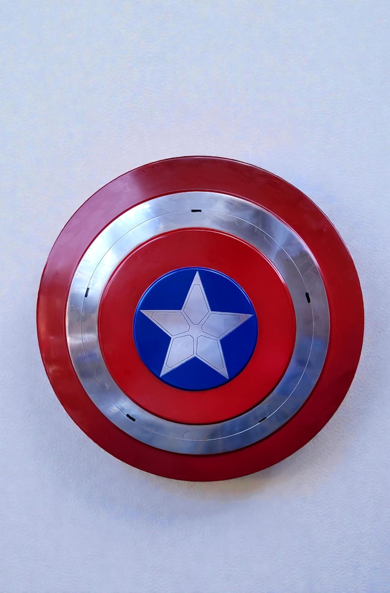 Puede incluir: Un escudo circular rojo, plateado y azul con un emblema de estrella blanca. El escudo tiene un anillo exterior rojo, un anillo central plateado y un centro rojo. Un c&iacute;rculo azul en el centro muestra una estrella blanca.