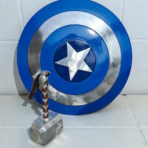 May include: A blue, silver, and white Captain America shield with a five-pointed star in the center. A silver and brown Thor's hammer is in front of the shield. The shield is approximately 24 inches in diameter.