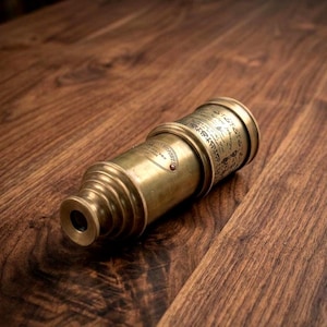 May include: A cylindrical brass telescope featuring a tapered eyepiece and a main barrel adorned with intricate engraved text and decorative patterns. The metal surface displays a weathered, aged finish with visible metallic textures and details.
