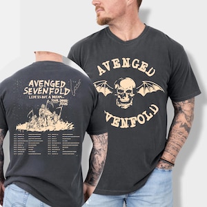 May include: Dark grey t-shirt with the band name "Avenged Sevenfold" and a skull with bat wings. The back of the shirt shows "Avenged Sevenfold", "Life is but a dream... Tour 2026" and a list of tour dates.