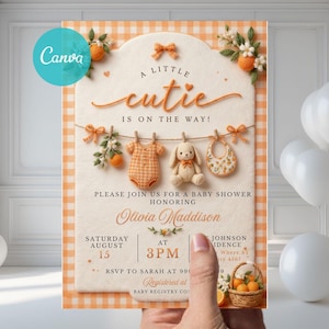 Könnte beinhalten: Babyparty-Einladung mit hellorangefarbenem und weißem Vichy-Muster. Die Einladung enthält den Text "A little cutie is on the way!" und enthält einen Baby-Strampler, ein Stoffkaninchen und ein Lätzchen. Die Einladung wird von einer Hand gehalten.