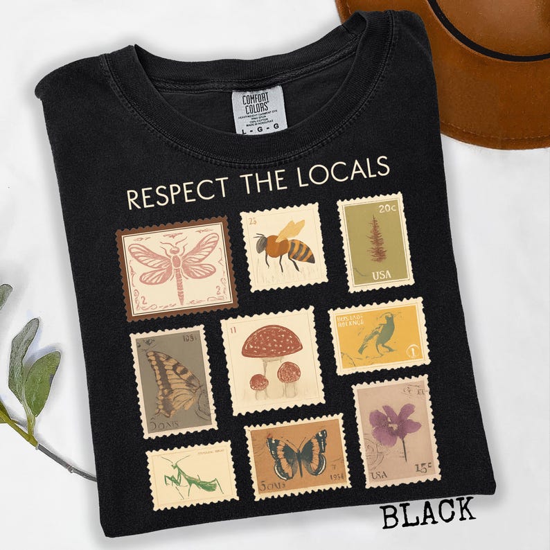 May include: Black t-shirt with the text "RESPECT THE LOCALS" and a design of postage stamps featuring insects, plants, and flowers. The word "BLACK" is printed at the bottom of the shirt. The shirt is made of a soft material.