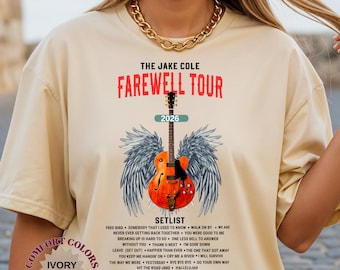 May include: Ivory-colored t-shirt featuring "THE JAKE COLE FAREWELL TOUR 2026" in red text. The design includes a guitar with angel wings and a setlist. The shirt is made of Comfort Colors material.