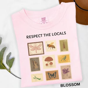 May include: A light pink t-shirt with the text "RESPECT THE LOCALS" and the word "BLOSSOM". The shirt features a collection of postage stamp designs with insects, mushrooms, and flowers.