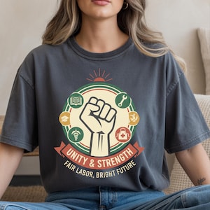 May include: Dark grey t-shirt featuring a graphic with a raised fist, surrounded by icons of a book, graduation cap, medical symbol, wrench, and more. The text reads "Unity & Strength, Fair Labor, Bright Future."