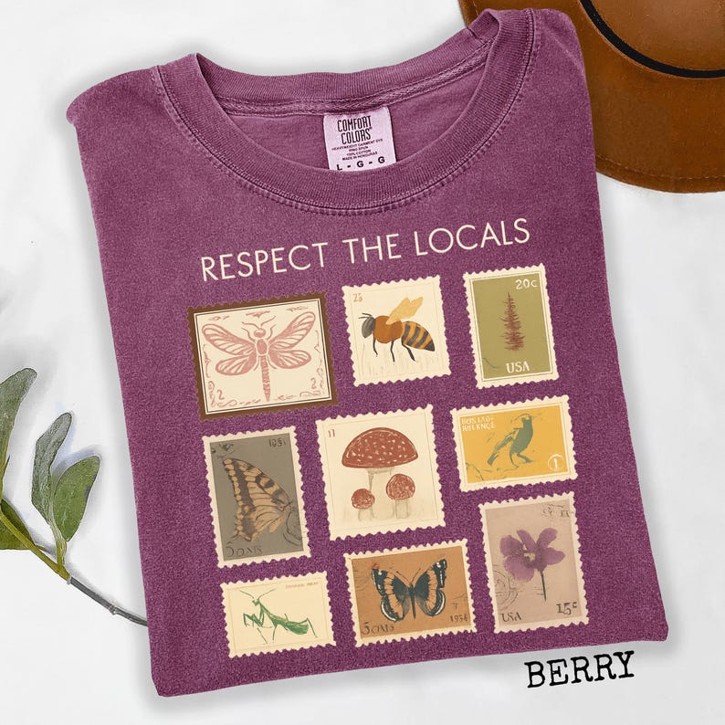 May include: Berry-colored t-shirt with the text "RESPECT THE LOCALS" and various postage stamp designs featuring insects, mushrooms, and flowers. The shirt has a crew neck and a Comfort Colors tag.