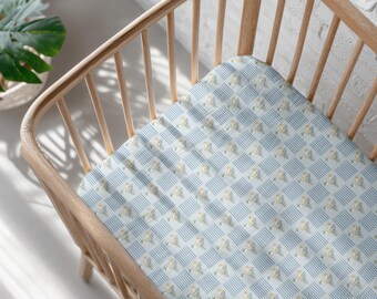 Peut inclure: Un lit bébé avec un drap-housse à motifs. Le drap présente un motif répétitif de rayures et de carrés bleu clair, chaque carré contenant de petits motifs floraux. Le lit est en bois clair.