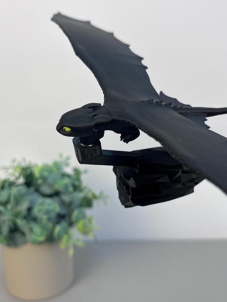 May include: A black dragon figurine with outstretched wings and yellow eyes. The dragon is mounted on a black base. The figurine is a detailed representation of a dragon, with textured wings and a sleek body. The dragon is a fantasy-themed item.