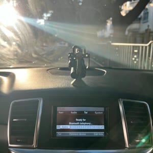 Pu&ograve; includere: Un cruscotto per auto con un supporto per telefono e un display digitale. Il display mostra l'ora, la navigazione, l'audio, il telefono e le opzioni di sistema. Lo schermo recita "Ready for Bluetooth telephony..." e mostra un numero di telefono.