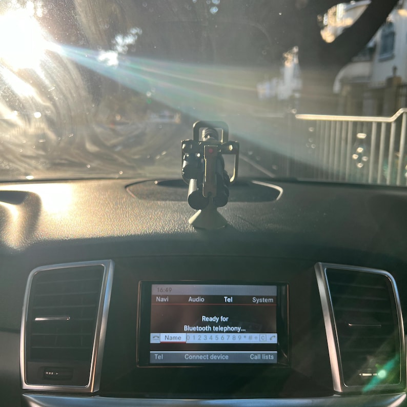 Pu&ograve; includere: Un cruscotto per auto con un supporto per telefono e un display digitale. Il display mostra l'ora, la navigazione, l'audio, il telefono e le opzioni di sistema. Lo schermo recita "Ready for Bluetooth telephony..." e mostra un numero di telefono.