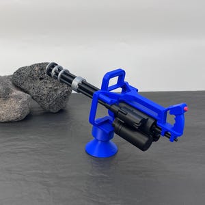 Pu&ograve; includere: Una minigun giocattolo blu e nera. La pistola presenta un design a canna rotante ed &egrave; montata su una base blu. L'impugnatura ha un pulsante rosso. Il giocattolo &egrave; realizzato in plastica ed &egrave; progettato per assomigliare a una vera minigun.