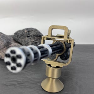 Pu&ograve; includere: Un modello in miniatura di mitragliatrice Gatling color oro, con canna nera e cilindro rotante argentato. Il modello &egrave; montato su una base color oro e posto su una superficie grigio scuro. La replica &egrave; dettagliata.