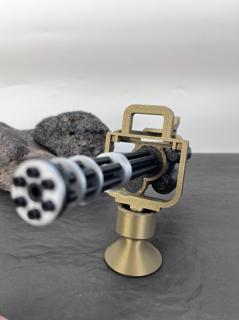 Pu&ograve; includere: Un modello in miniatura di mitragliatrice Gatling color oro, con canna nera e cilindro rotante argentato. Il modello &egrave; montato su una base color oro e posto su una superficie grigio scuro. La replica &egrave; dettagliata.