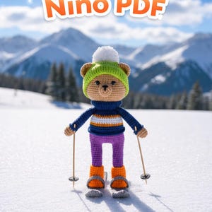 Può includere: Un orsetto all'uncinetto con cappello verde con pompon bianco, maglione a righe blu e arancioni, pantaloni viola e stivali arancioni, con bastoncini da sci. Il testo "Crochet Skier Bear Nino PDF" è visibile.