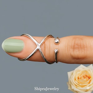 Könnte beinhalten: Ein silberfarbener Fingerring mit einem X-förmigen Design und zwei kleinen Kugelakzenten. Der Ring wird an einem Finger mit hellgrünem Nagellack getragen. Der Etsy-Shop-Name "ShipraJewelry" ist unten sichtbar.