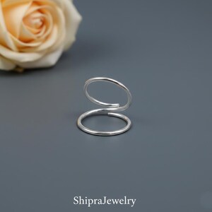 May include: A silver-colored metal ring featuring a double-loop bypass design with two open ends. The ring has a smooth, polished finish and a simple, continuous wire-like structure. The text ShipraJewelry is printed at the bottom of the image.