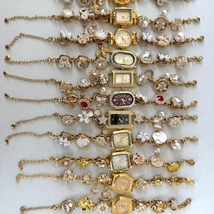 Puede incluir: Una colección de relojes de pulsera dorados con varios elementos decorativos, incluyendo perlas, cristales y diseños florales. Las esferas de los relojes tienen diferentes formas, como redondas, rectangulares y ovaladas.