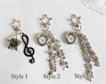 May include: Three silver-toned keychain charms. Style 1 features a star-shaped watch and a black treble clef. Style 2 has a heart-shaped watch with star-shaped chain accents. Style 3 has a heart-shaped watch with a beaded chain.