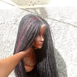 May include: A black braided wig with red highlights is displayed on a mannequin head. The wig features long, micro braids and a lace front. The mannequin is wearing a gold necklace. The background is a textured, light-colored wall.