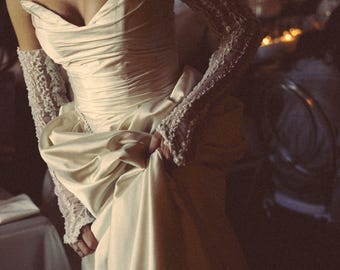 May include: Ivory satin wedding gown with a sweetheart neckline and draped bodice. The dress features a full skirt and is paired with lace gloves. The overall style is elegant and classic, suitable for a formal event.