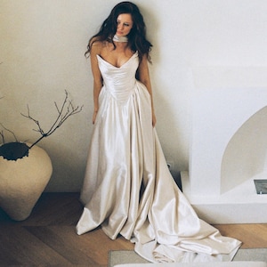 Puede incluir: Vestido de novia marfil sin tirantes con escote coraz&oacute;n y falda fluida. El vestido presenta un corpi&ntilde;o ajustado y una larga cola. La novia lleva un choker marfil a juego. El vestido es de sat&eacute;n.