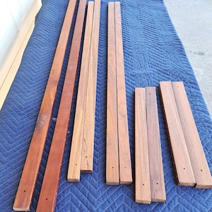May include: A set of eight wooden slats, likely teak, in various lengths. The slats are a rich reddish-brown color and have a smooth, polished finish. They appear to be part of a furniture project or a DIY craft.