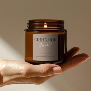以下が含まれることがあります： 金属の蓋が付いた茶色のガラス瓶のキャンドル。ラベルには「Cinnamon Vanilla」と書かれています。キャンドルは香り付きキャンドルで、237gです。手で持っています。