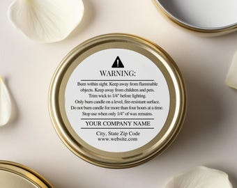 May include: A gold-colored candle tin with a white label featuring safety warnings and company information. The label includes text about burning the candle safely. White petals are scattered around the tin.