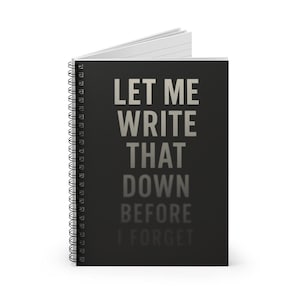 May include: A black spiral-bound notebook with the text "LET ME WRITE THAT DOWN BEFORE I FORGET" in white and gray lettering. The notebook is open, revealing white lined pages.