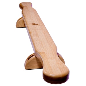 May include: A light brown bamboo longboard with a curved deck and a logo. The longboard is supported by two curved wooden stands. The wood grain is visible on the board and stands.