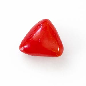 May include: A vibrant, triangular, red gemstone with a smooth, polished surface. The gem is set against a clean white background, highlighting its shape and color. This could be a decorative element or a component of jewelry.