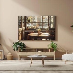 May include: A modern living room with a large framed picture of a cafe scene above a wooden cabinet. The room features a light beige color scheme, a white armchair, and several potted plants. A small, round coffee table sits in front of the armchair.