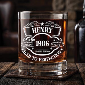 May include: A clear glass tumbler filled with amber liquid, featuring white etched text that reads HENRY, No 1986, ORIGINAL QUALITY, LIMITED EDITION, and AGED TO PERFECTION, arranged within a decorative frame with stars and scrollwork elements.