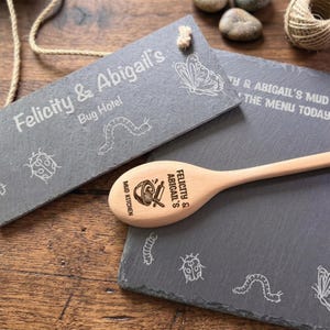 May include: Two rectangular grey slate plaques and a light-coloured wooden spoon. One plaque reads Felicity & Abigail's Bug Hotel with insect engravings. The other reads Felicity & Abigail's Mud Kitchen. The spoon features a mixing bowl graphic.