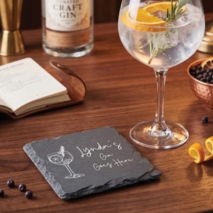 May include: A slate coaster with the text "Lynda's Gin Goes Here" and a cocktail glass illustration. A gin cocktail with orange and rosemary sits in a large glass. A bottle of craft gin and a copper bowl are also visible.