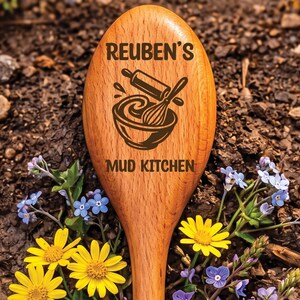 May include: Wooden spoon with the text "REUBEN'S MUD KITCHEN" and a graphic of a bowl, rolling pin, and whisk. The spoon is surrounded by soil, yellow and blue wildflowers.