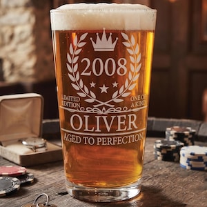 Op de afbeelding: Een helder glazen bierglas gevuld met amberkleurige vloeistof en wit schuim, voorzien van een gegraveerd ontwerp met een kroon, het jaar 2008, de naam OLIVER en de tekst LIMITED EDITION, ONE OF A KIND en AGED TO PERFECTION in witte letters.