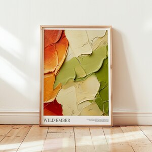 Puede incluir: Una impresión artística abstracta enmarcada con gruesas pinceladas en tonos naranja, verde y crema. La obra se titula "WILD EMBER" en texto blanco en la parte inferior. El marco es de color madera clara y la impresión se muestra contra una pared blanca.