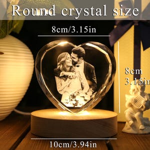 May include: A heart-shaped crystal with a photo of a couple, illuminated by a wooden base. The crystal measures 3.15 inches in height and width, and 3.94 inches in base length. The text on the image reads "Round crystal size".
