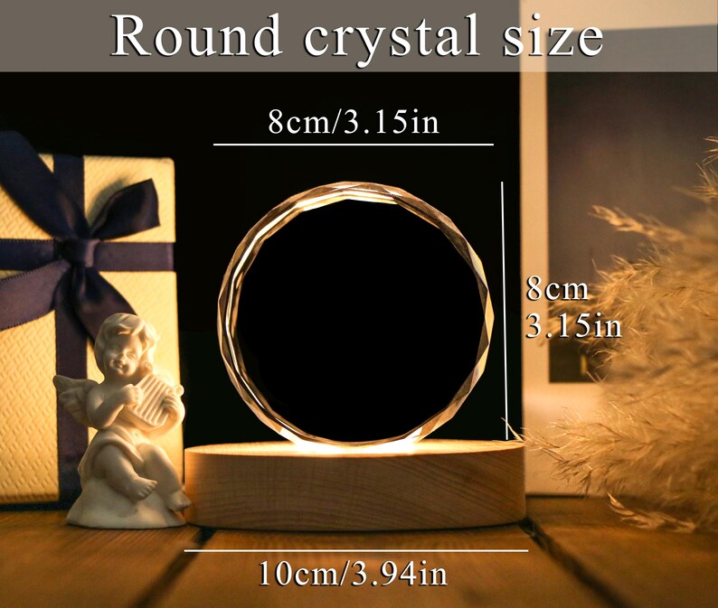 May include: A round crystal with a faceted design, illuminated from below, sits on a wooden base. The crystal is 3.15 inches in diameter and 3.94 inches wide. The text "Round crystal size" is at the top. A small angel statue and a gift box are in the background.