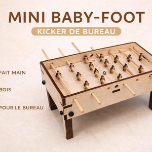 Könnte beinhalten: Kleiner Tischfußballtisch aus hellem Holz mit dunkelbraunen Beinen und Holzfiguren. Der Text "MINI BABY-FOOT" und "KICKER DE BUREAU" ist sichtbar. Das Bild enthält auch die Texte "FAIT MAIN", "BOIS" und "POUR LE BUREAU".