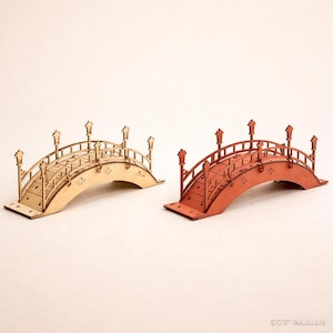 Peut inclure: Deux ponts décoratifs en bois. L'un est de couleur bois naturel, l'autre est peint en rouge-orangé. Les deux ont des conceptions arquées avec des garde-corps décoratifs et des lampadaires. Les ponts sont parfaits pour les scènes miniatures ou l'artisanat.