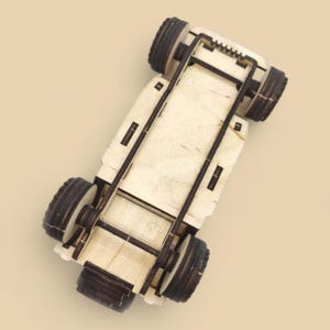 May include: A wooden toy car with four dark brown wheels and a light brown body. The car's underside is visible, showing the wooden frame and axle supports. The toy is designed with a simple, geometric aesthetic.