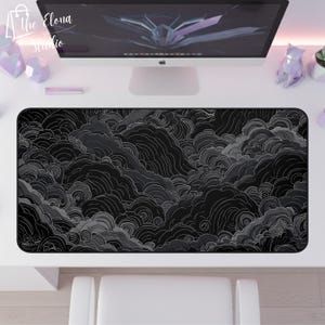 May include: Black and gray desk mat with a cloud-like pattern. The mat is rectangular and covers a large portion of the desk. The design features swirling, layered shapes in shades of gray and black, creating a textured appearance. The Elona Studio logo is in the top left corner.