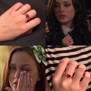 May include: A gold ring featuring a heart-shaped red gemstone set in the center. The band has a textured, decorative design on both sides of the stone. The ring is shown worn on a finger in multiple views, highlighting the red heart-shaped stone.