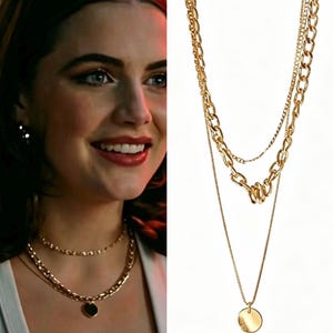 May include: A multi-layered gold-tone necklace featuring a combination of delicate link chains and a thicker cable chain. The design includes a small, smooth, circular gold pendant suspended from the longest chain, creating a tiered appearance.